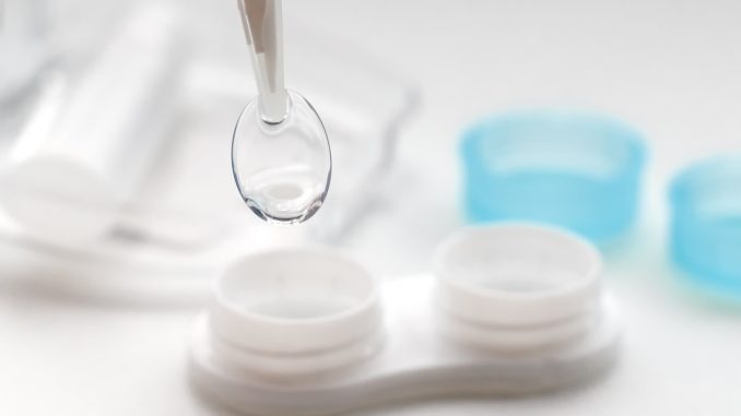 Tweezers with contact lens and plastic container on white background
